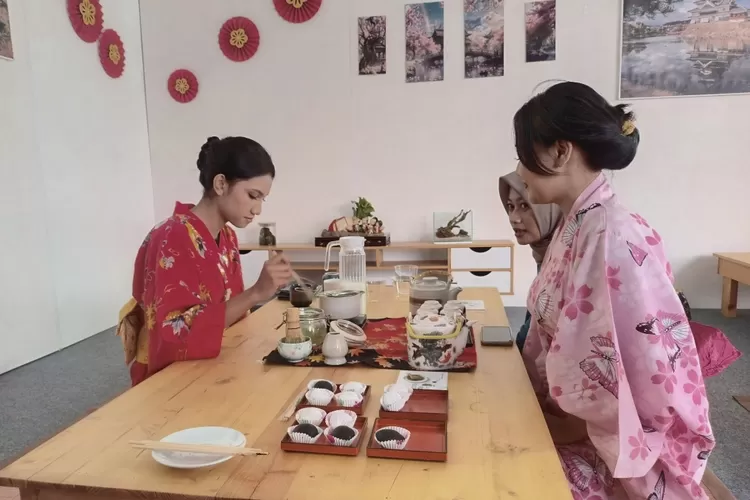 Dua wanita mengenakan kimono duduk berhadapan di meja kayu, menikmati hidangan dan teh dalam suasana ruangan yang estetik khas Jepang, menggambarkan kehangatan dan kenyamanan lingkungan perumahan siap huni di Semarang.